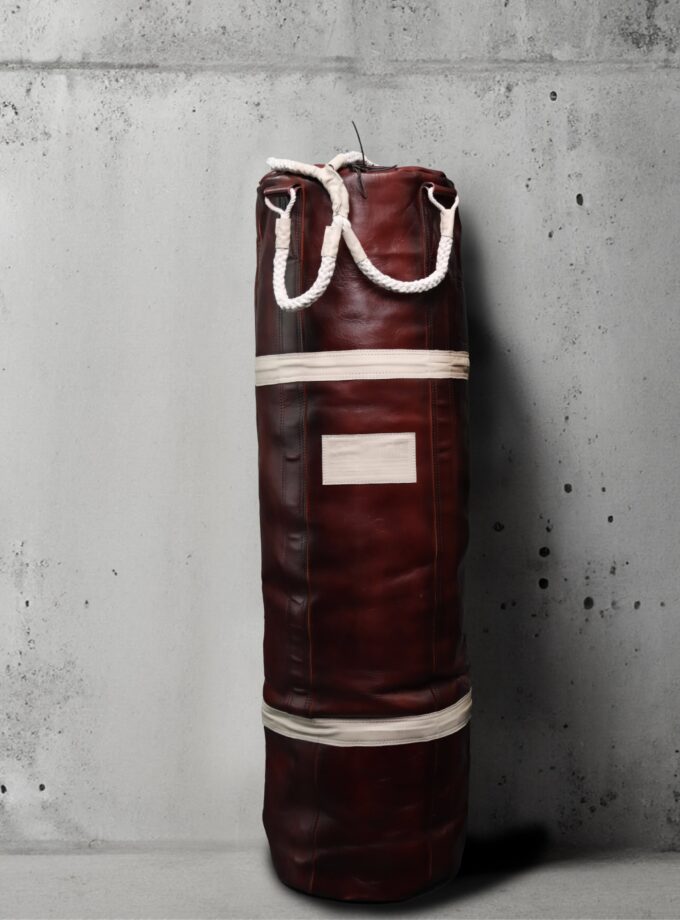 4’ Weave Warrior Punching Bag in Crimson & Ivory against a concrete wall.